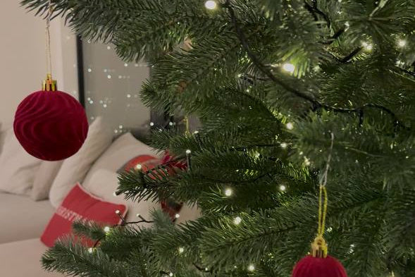 Bordó bársony karácsonyfadíszek meleg fehér fényfüzérrel díszített zöld műfenyőn, otthonos nappaliban